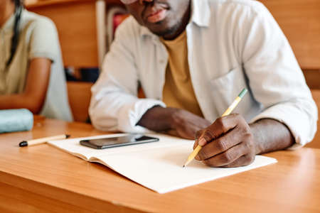 Close-up of African student sitting at desk and writing exam at universityの写真素材