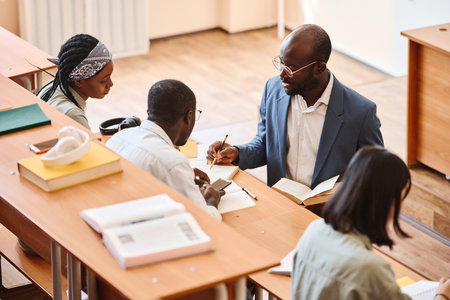 Teacher giving advice to student in his task while they sitting at desk in auditoriumの写真素材