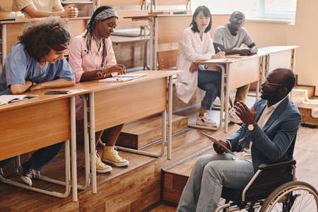 African teacher with disability sitting on wheelchair and reading lecture for medical students at universityの写真素材