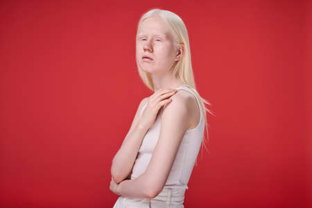 Portrait of albino girl with unusual appearance and natural beauty standing against red backgroundの写真素材