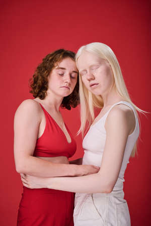 Portrait of two girls with unusual appearances embracing against red backgroundの写真素材