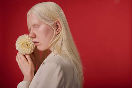 Portrait of young girl with unusual appearance posing with white flower against red backgroundの写真素材