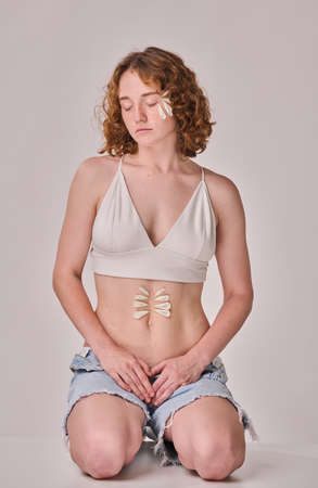 Portrait of ginger young girl with petals on her body sitting against white backgroundの写真素材