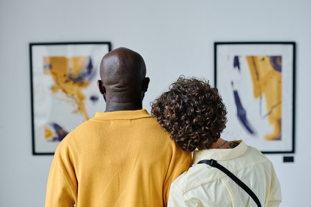 Rear view of multiethnic young couple embracing and enjoying art together at galleryの写真素材