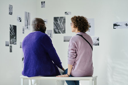 Rear view of young couple having date at art gallery, they sitting and talking to each other
