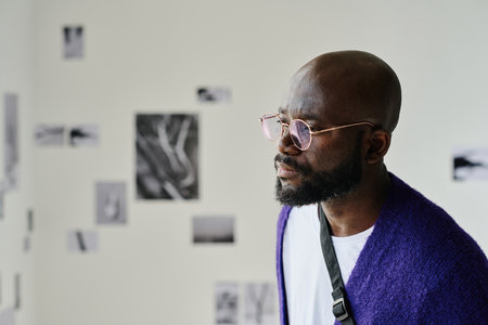 Close-up of African young man in eyeglasses examining modern art on wall at gallery