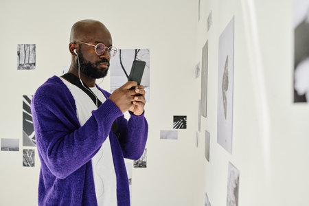 African man in headphones using smartphone while visiting art galleryの写真素材