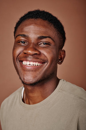 Portrait of happy African teenage boy smiling at camera isolated on brown background