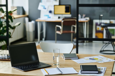 Workplace of economist or accountant with laptop, notebook with pen, glass of water and financial documents in openspace officeの写真素材