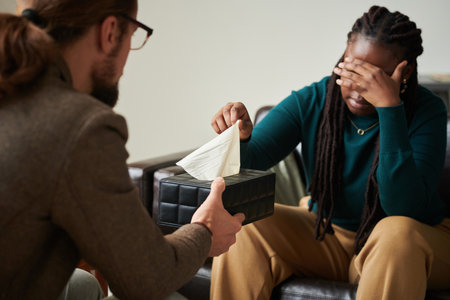 Psychiatrist giving tissues to depressed patient while she sitting on sofa during consultation at officeの写真素材