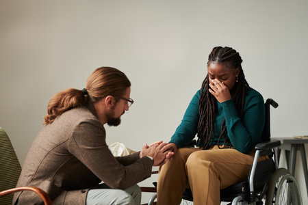 Psychotherapist holding hand with patient with disability and supporting her during rehabilitationの写真素材
