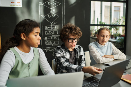 Group of children discussing software on computer at desk during IT lesson