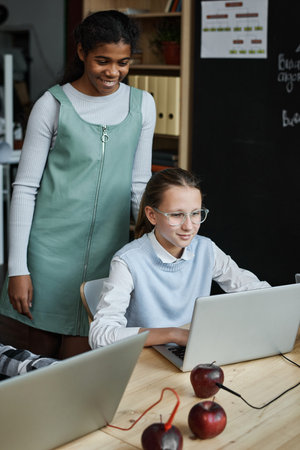 Two schoolgirls using computer in team at table at lesson, they looking at computer monitor and...