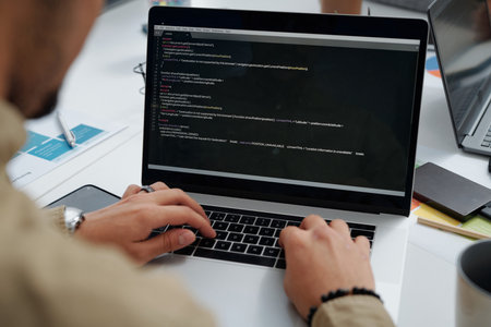 Close-up of young developer writing codes on computer while working at table at IT officeの写真素材