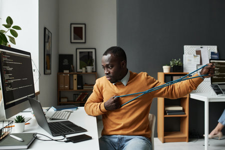 African American IT programmer training with rubber band while working with computer program on computer at his workplaceの写真素材