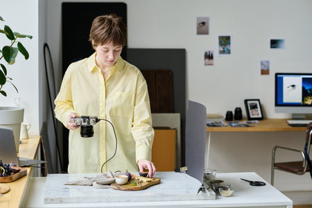 Young photographer taking picture of food on tray using her professional camera during her work in...