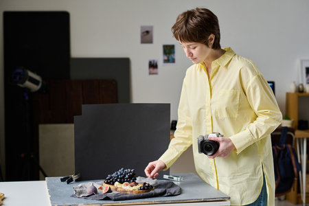 Young photographer decorating dish with fruits for professional shooting on camera in studioの写真素材