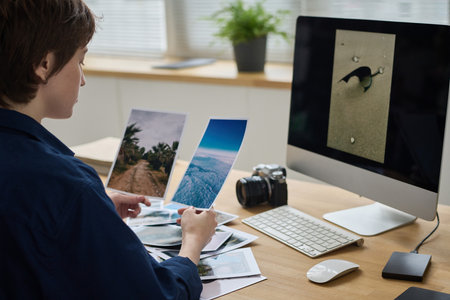 Young photographer sitting at her workplace in front of computer monitor and examining professional picturesの写真素材