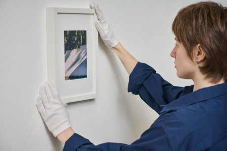 Young woman in gloves hanging framed photo on the white wallの写真素材