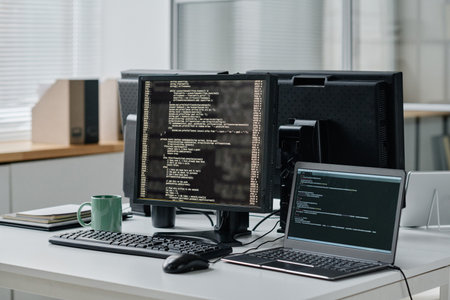 Workplace of developer with computer and laptop with codes on screens in modern officeの写真素材