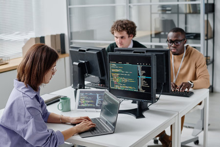 Group of young people sitting at their workplace and writing codes on computers, they working in IT...