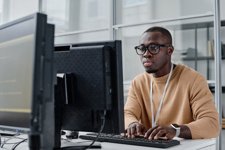 African American programmer in eyeglasses concentrating on his online work on computer, he typing...