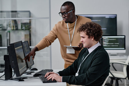 Two young colleagues developing new code for computer program in team in modern office