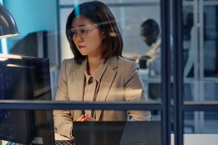 Asian young businesswoman in suit concentrating on her work on computer at her workplace in officeの写真素材