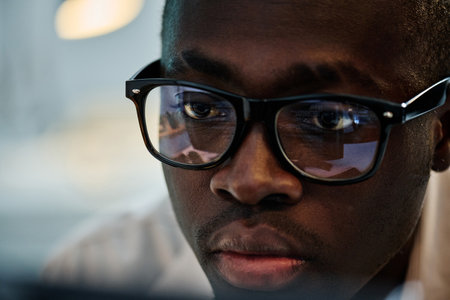 Close-up of African American in eyeglasses concentrating on his online work , he examining computer...