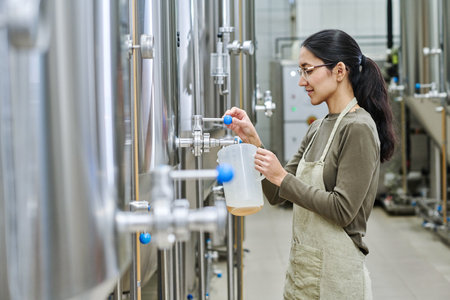Worker pouring brewed beer in container for degustation during her work in brewery plant
