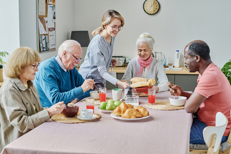 Young caregiver serving senior people at table, they sitting at table and eating food and she setting the tableの写真素材