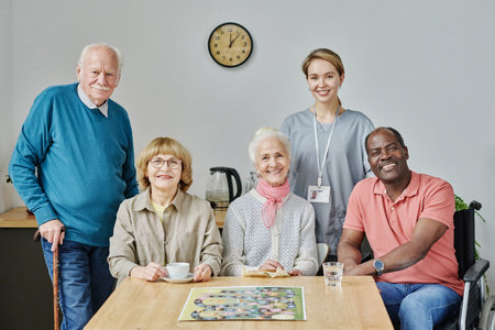 Portrait of senior people with caregiver smiling at camera while playing board game