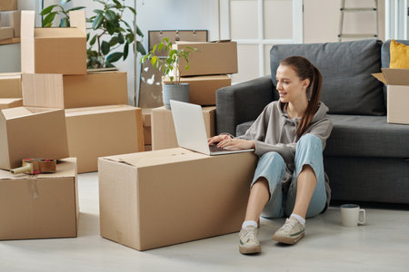 Young woman sitting on the floor in the room and using laptop, she searching for new flat to rent