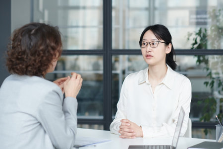 Asian young candidate sitting at table and talking to interviewer during job interview