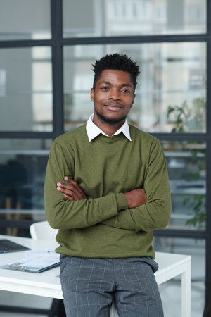 Portrait of young African American businessman standing with his arms crossed near his workplace and looking at cameraの写真素材