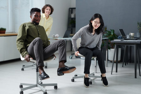 Group of business colleagues fooling around together on chairs in office during breakの写真素材