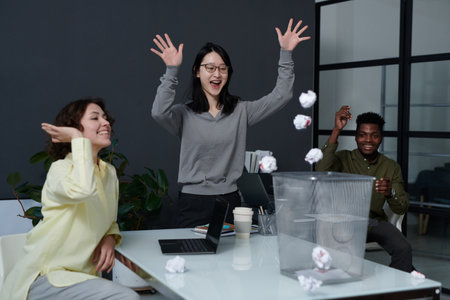 Group of business people fooling around in office throwing paper balls in basketの写真素材