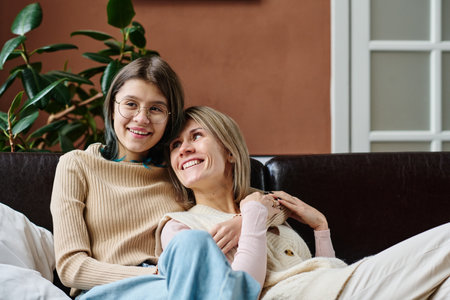 Happy teenage girl embracing her mother and smiling while they resting on sofa in the roomの写真素材