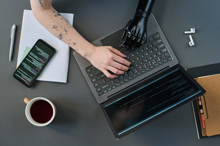 High angle view of girl with prosthetic arm typing on laptop at table to do online work