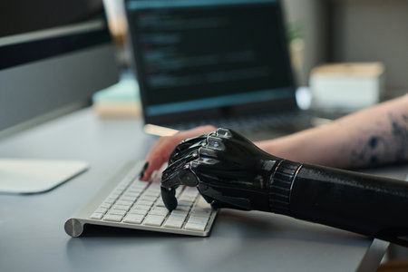 Close-up of girl with prosthetic arm typing on keyboard, she using computer to do online workの写真素材