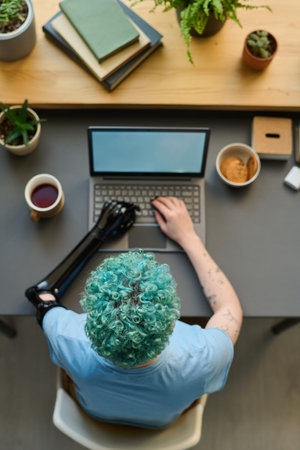 High angle view of young girl with prosthetic arm typing on laptop sitting at her workplaceの写真素材