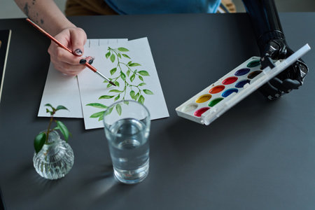 High angle view of woman with prosthetic hand painting picture with paints and brushの写真素材