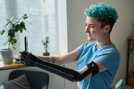 Young blogger with prosthetic arm using smartphone to talk to her followers during online broadcastの写真素材