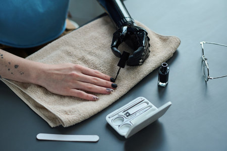 Close-up of young woman with prosthetic hand doing manicure to herself, she painting her nails with varnishの写真素材