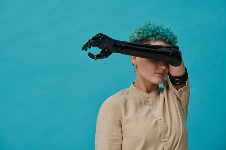 Portrait of young girl with prosthetic arm in depression standing against blue backgroundの写真素材