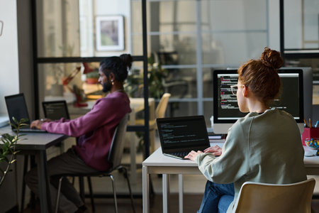 Young programmers sitting at their workplaces and typing codes for new software on computers in IT officeの写真素材