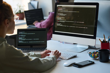 Rear view of young programmer typing security code on computer sitting at her workplace in front of monitorの写真素材
