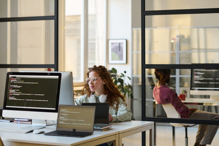 Young people sitting at their workplaces and working with security codes on computers in IT officeの写真素材
