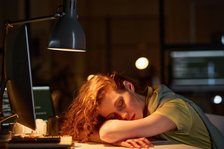 Tired female programmer sleeping at her workplace with computer during her deadline in officeの写真素材