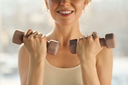Close-up of young healthy woman exercising with dumbbells and smiling at cameraの写真素材